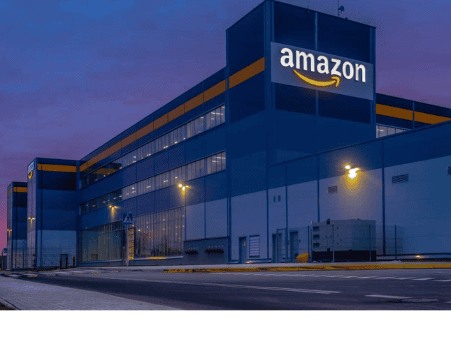  Amazon UK warehouse building at dusk with logo visible.